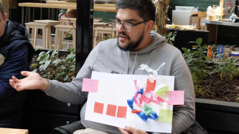 Teacher in grey shirt hold a piece of white paper with colourful post-its and raises his arm as he  takes part in Creative Teacher CPD session with Young at Art.