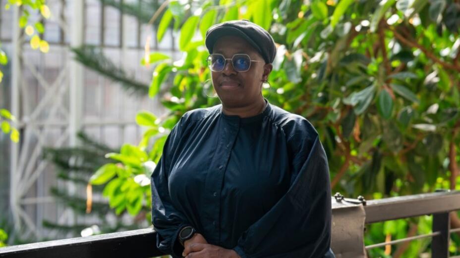 Artist Ain Bailey stands in front of a leafy background.
