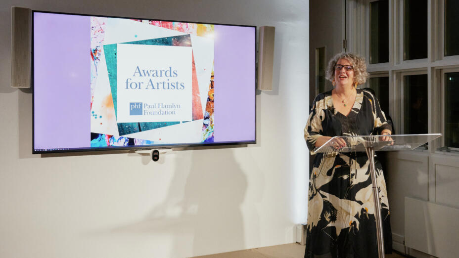 Moira Sinclair, Chief Executive of Paul Hamlyn Foundation, stands at a podium in front of a screen that says: Awards for Artists.