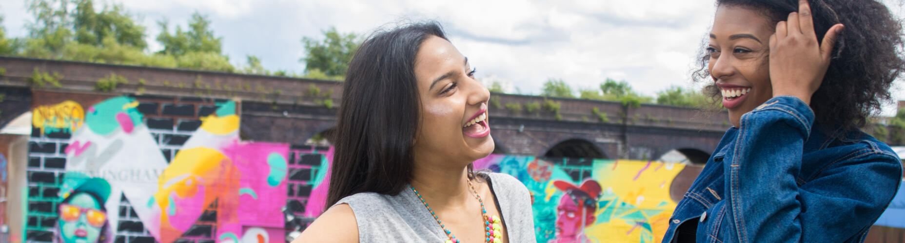 Two young people laughing in front of a wall with graffiti on it. Photo credit: Kieran, Beatfreeks Associate