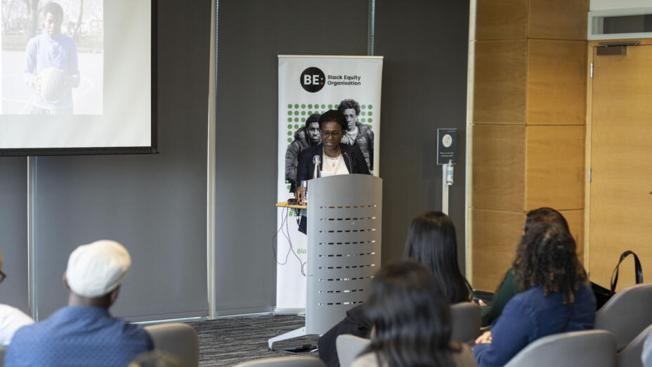 A woman stands up and gives a speech at an event organised by the Black Equity Organisation.
