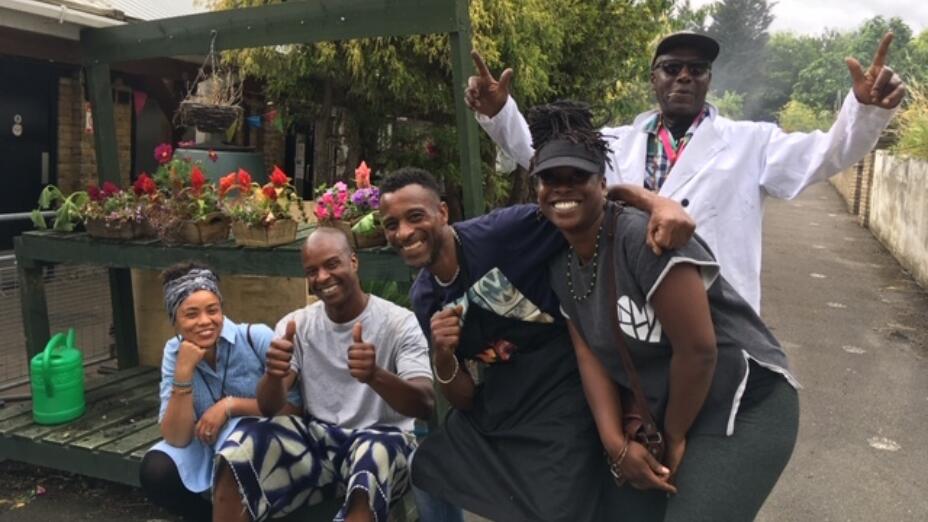 Group of people smiling in front of flowers beds at Wolves Lane Horticultural Centre - part of Ubele Initiative's Black Rootz, a multigenerational Black-led growing project.