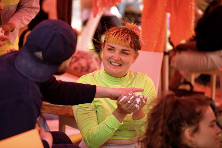 A young person in a bright green shirt is in conversation, holding foam as part of an interactive exercise