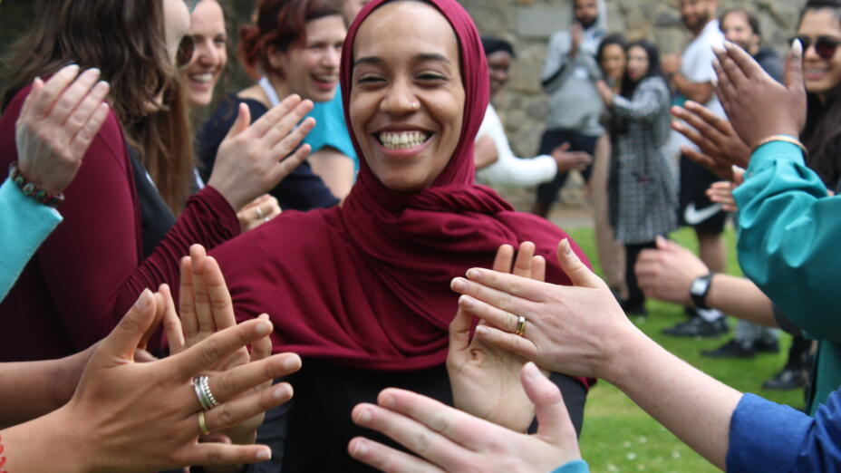 Young woman in a burgundy headscarf smiles as she gives high fives to her classmates at a Campaign Bootcamp graduation event outdoors.