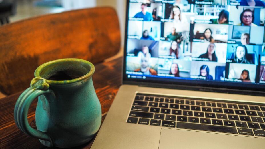 Blue ceramic coffee cup next to a silver laptop with a zoom meeting on the screen.