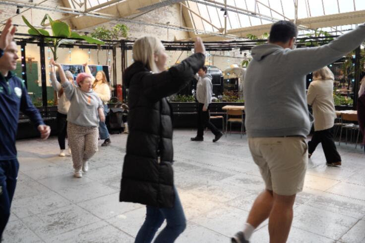 Several teachers walk in a circle with one arm raised as they take part in a Creative Evaluation Day as part of the Young at Art project.