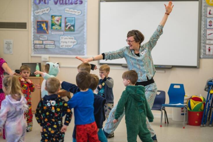 Group of young children in brightly coloured outfits take part in Wise About Words session joyously led by artist practitioner Sarah.