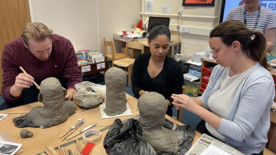 An artist practitioner works on clay busts with a male and female teacher.