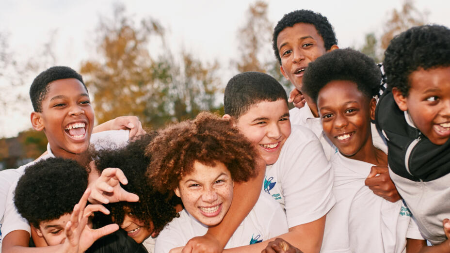A group of young boys are smiling and holding onto each other outdoors, facing the camera for a group shot