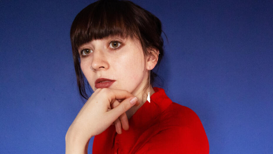Francesca Pidgeon (Dilettante) in red shirt against a bright blue background.