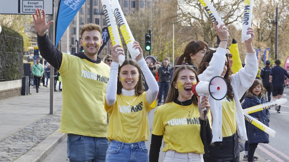 Three young people in yellow YoungMinds stand outdoors at a demo smiling and facing the camera - one holds a megaphone