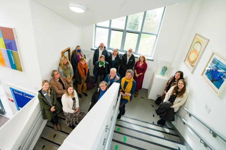 View from above of a group of about 15 teachers standing on a white staircase in the Newlyn In School Gallery. There are many large and bright artworks by students on the white walls.