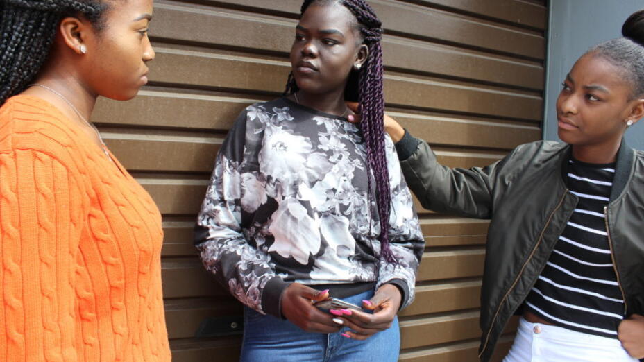 Three young girls are standing outside, in conversation