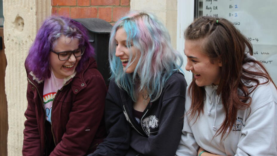 Three young people are sitting outside, laughing with each other