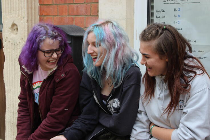 Three young people are sitting outside, laughing with each other