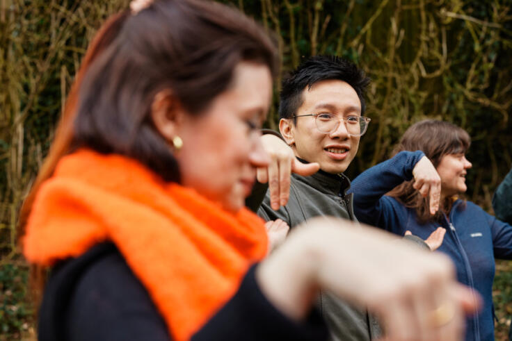 Group of three adults in the woods, smiling and playing a game.