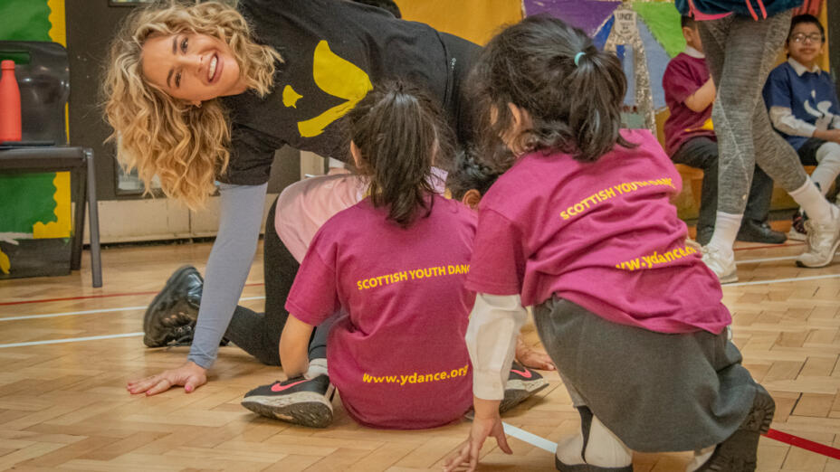 Woman with blonde hair leads dance-based learning session with primary school pupils as part of Step It Up, supported by the Teacher Development Fund.