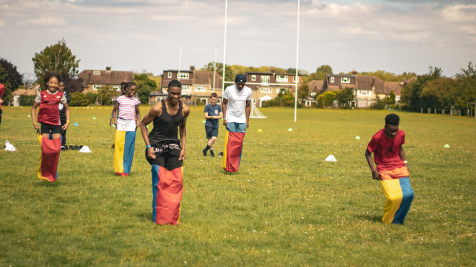 Group of young people playing on a sunny day in a park, wearing sacks and having a jumping race.