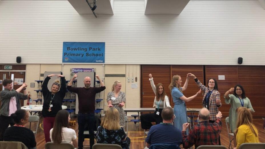 A large group teachers dance and take part in an arts-based learning cpd session in a school assembly hall.
