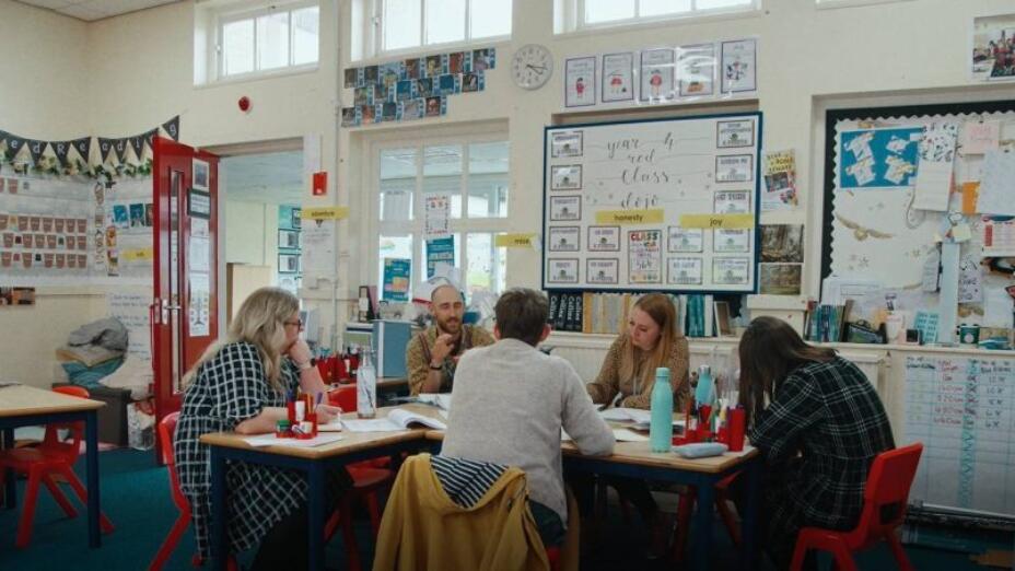 Teachers and artists take part in reflective session in a primary classroom with colourful decorations on the wall. Photo: brettinthecity.