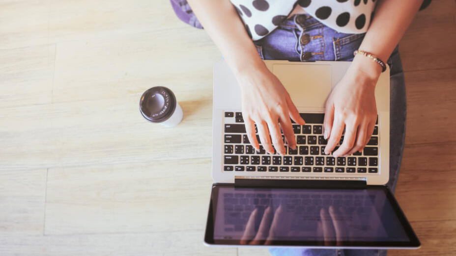 Woman wearing a black and white polka dot top with jeans types on a laptop that's on her lap.