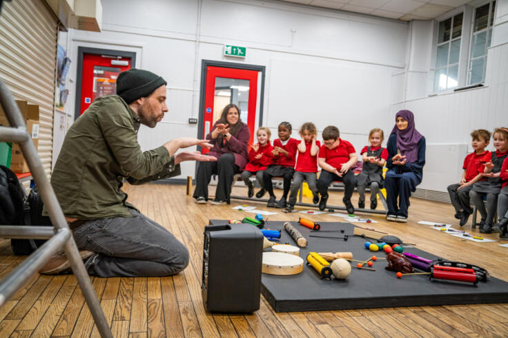 Artist working in a classroom with children in red uniforms as part of the Parallel Rhythms project.