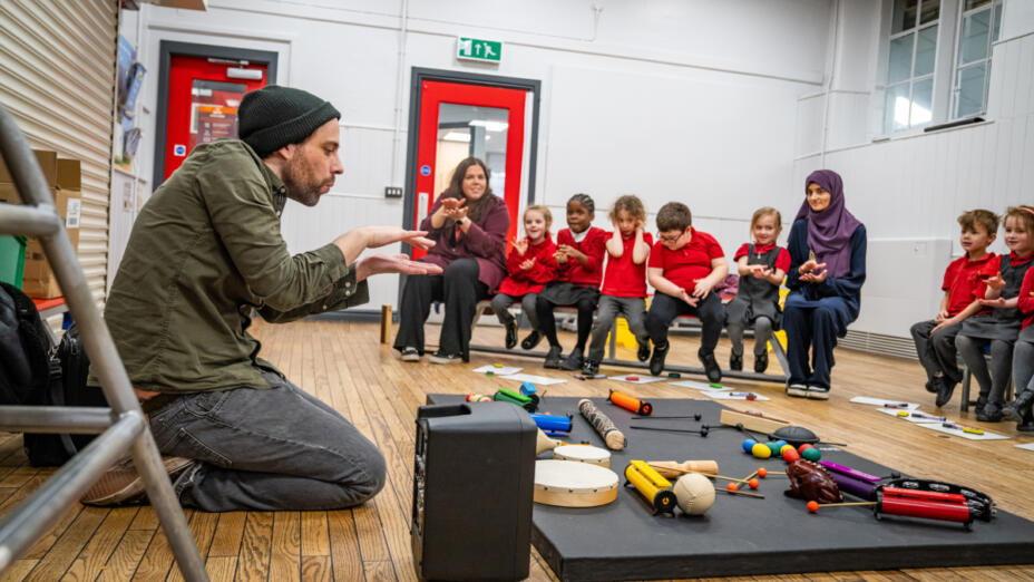 Artist working in a classroom with children in red uniforms as part of the Parallel Rhythms project.