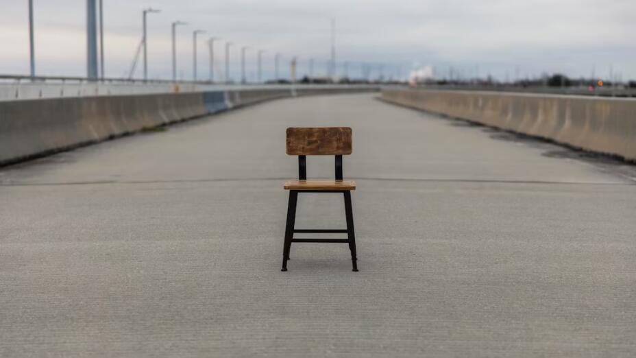Wooden school chair sitting in the middle of a road against a grey and isolated landscape
